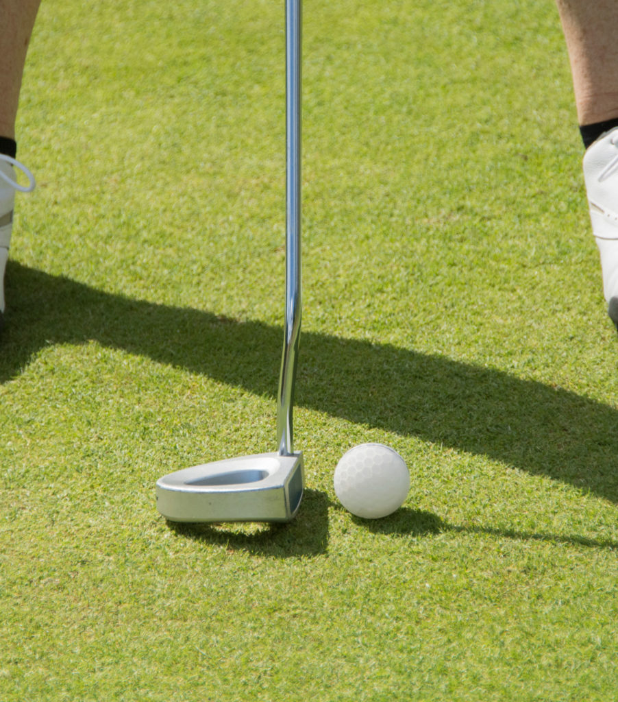 Golfer preparing to putt a golf ball on a green course, focus on putter and ball.