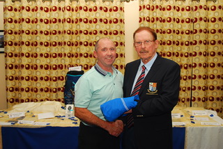 Two men shaking hands at an award ceremony with a decorated table in the background.