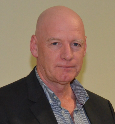 A person in a suit and collared shirt, posing against a neutral background, looking directly at the camera.
