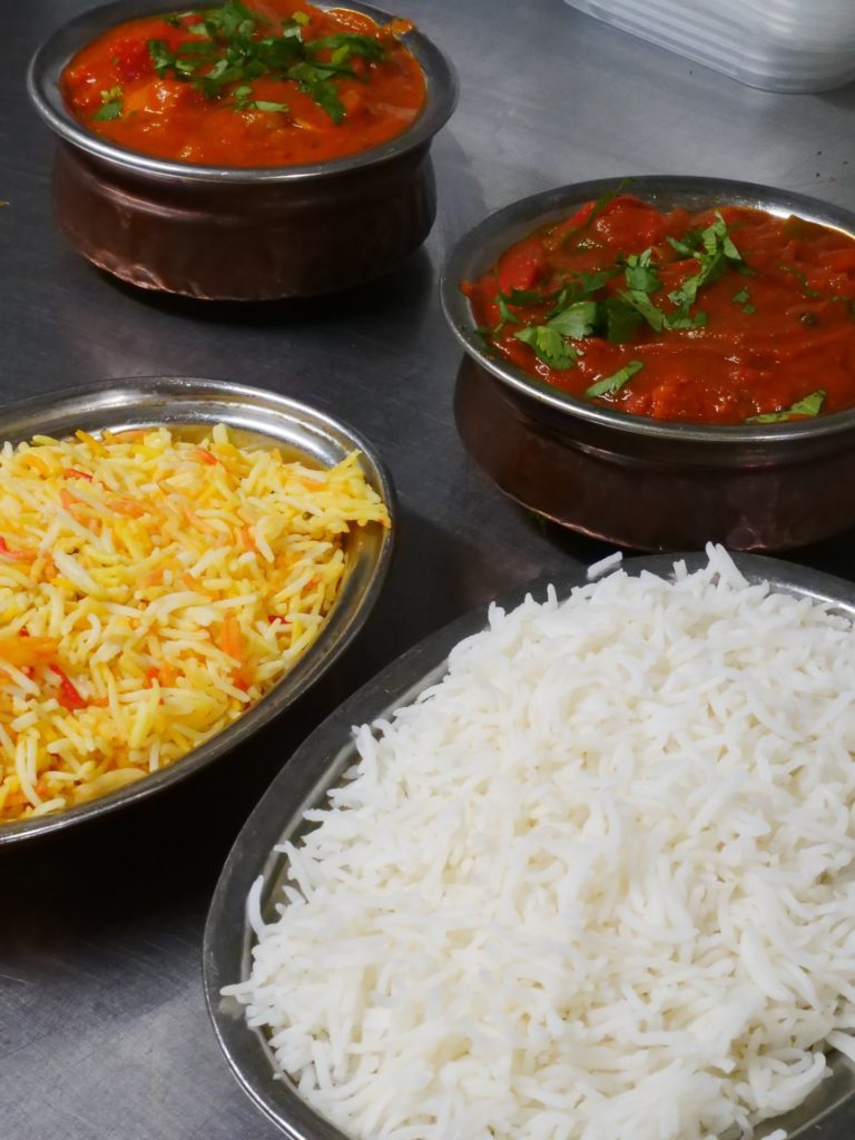Indian curries with vibrant red sauce served with fluffy rice and spiced rice, garnished with fresh herbs.