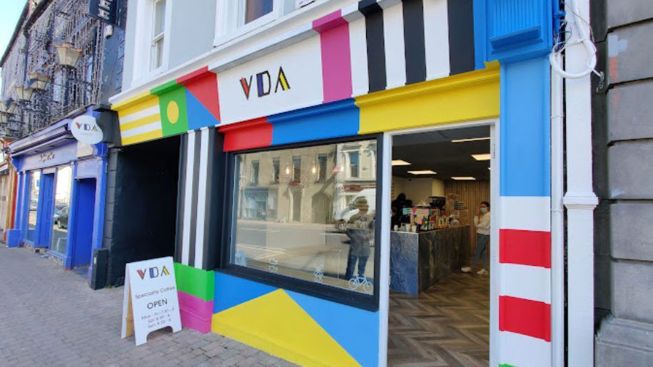 Vibrant exterior of a specialty coffee shop with geometric patterns and an open sign on a sunny street.