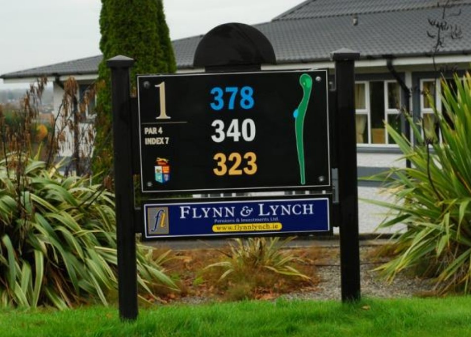 Golf hole sign with yardages and par information at course entrance with Flynn & Lynch advertisement below.