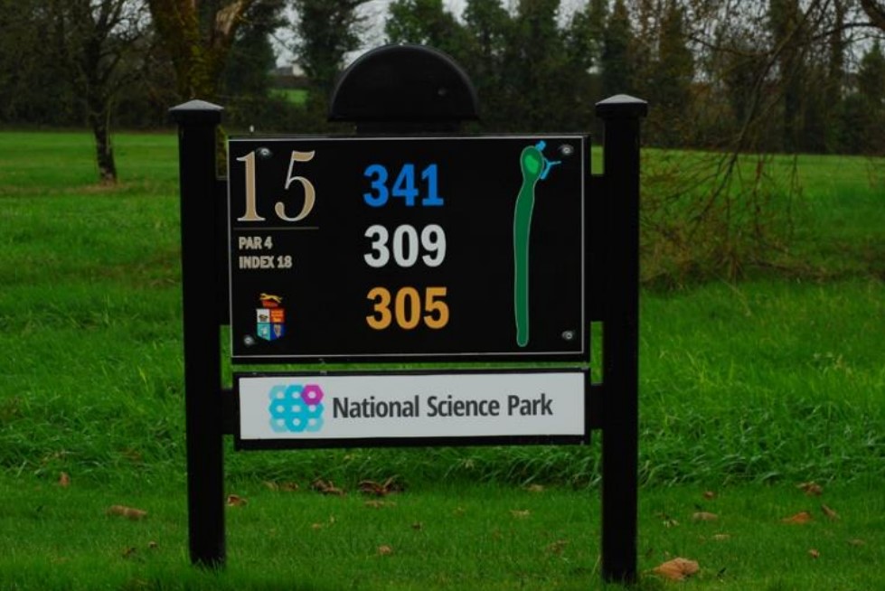 Golf course hole 15 sign at National Science Park, showing yardage details and par 4, with lush green background.
