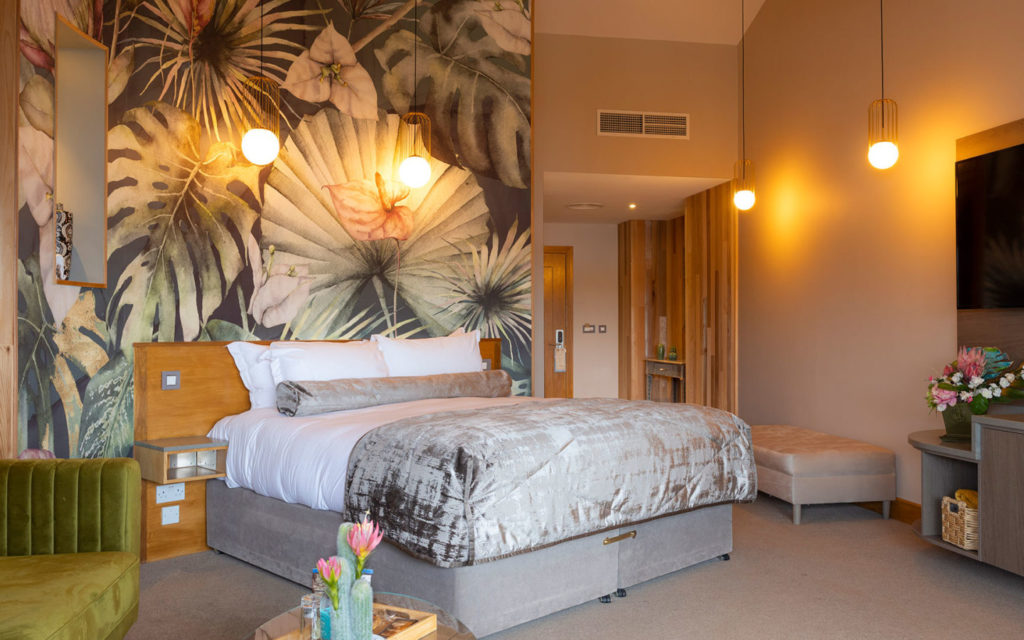 Luxurious hotel room with a tropical plant mural, modern lighting, and stylish decor.